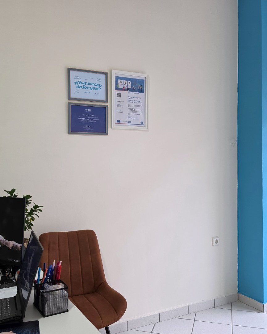 Ο τοίχος του γραφείου με τις κορνίζες και την αφίσα του προγράμματος